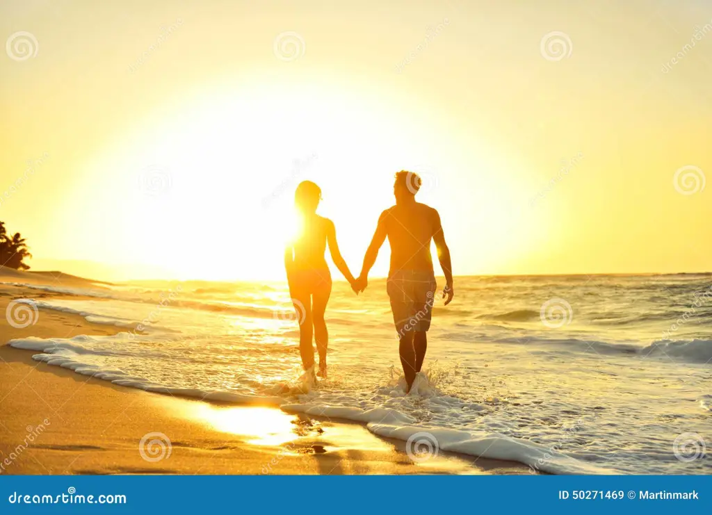 Pasangan di pantai saat matahari terbenam, melambangkan akhir yang indah