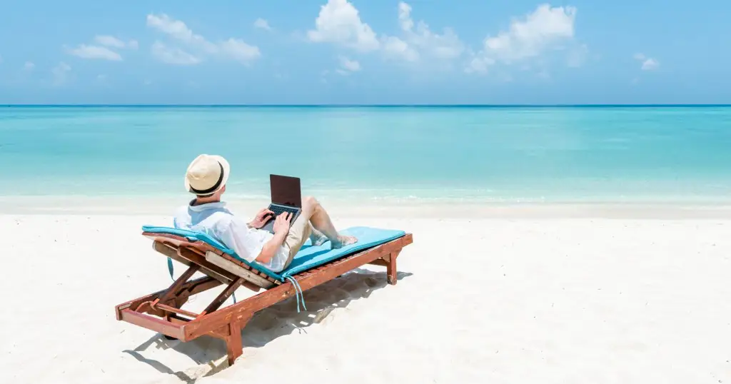 Seorang digital nomad bekerja di laptop di pantai