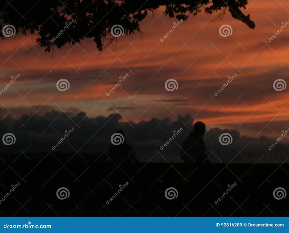 Siluet orang-orang di bawah langit senja yang berawan